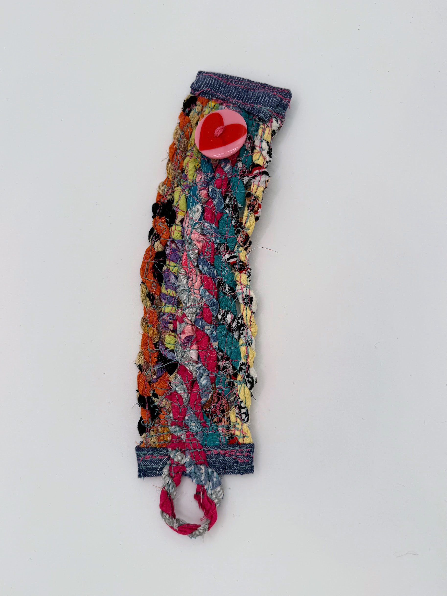 Handmade heart-button textile cuff laid flat with a braided loop