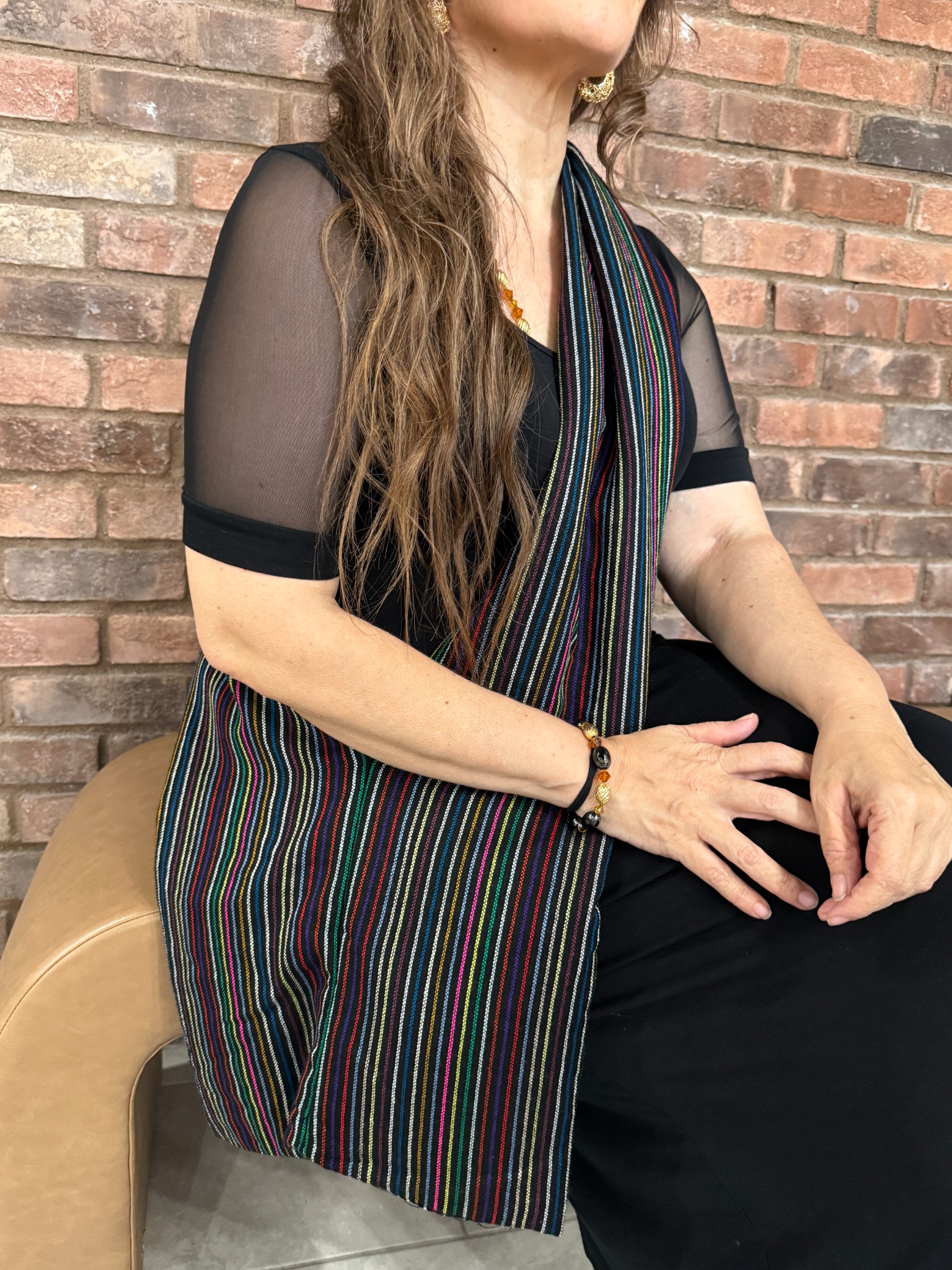 Woman wearing a long multicolored Vive Bonito textile piece against a brick wall